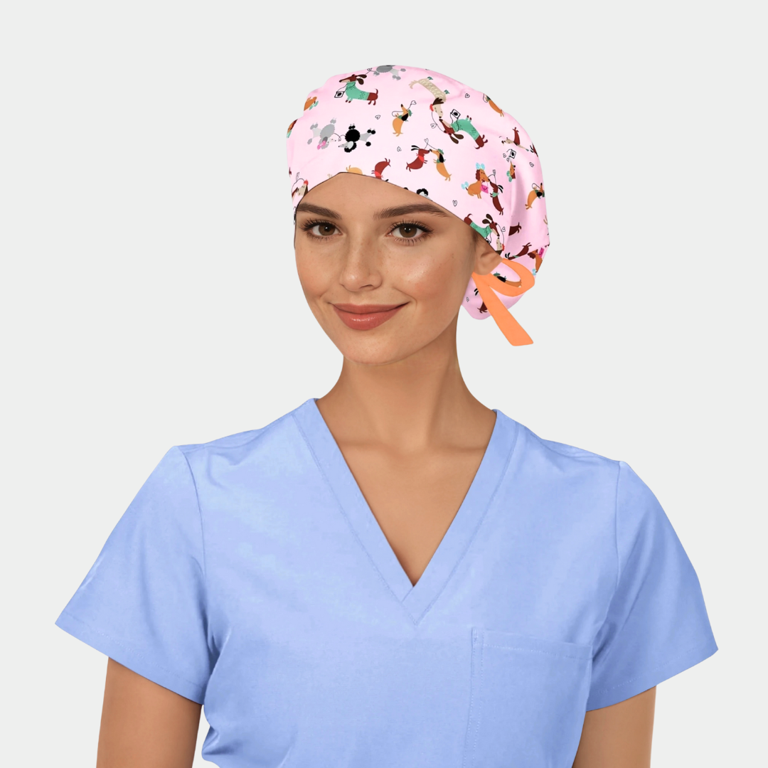 Person wearing a light blue scrub top and a pink scrub cap with dogs on it on a plain background