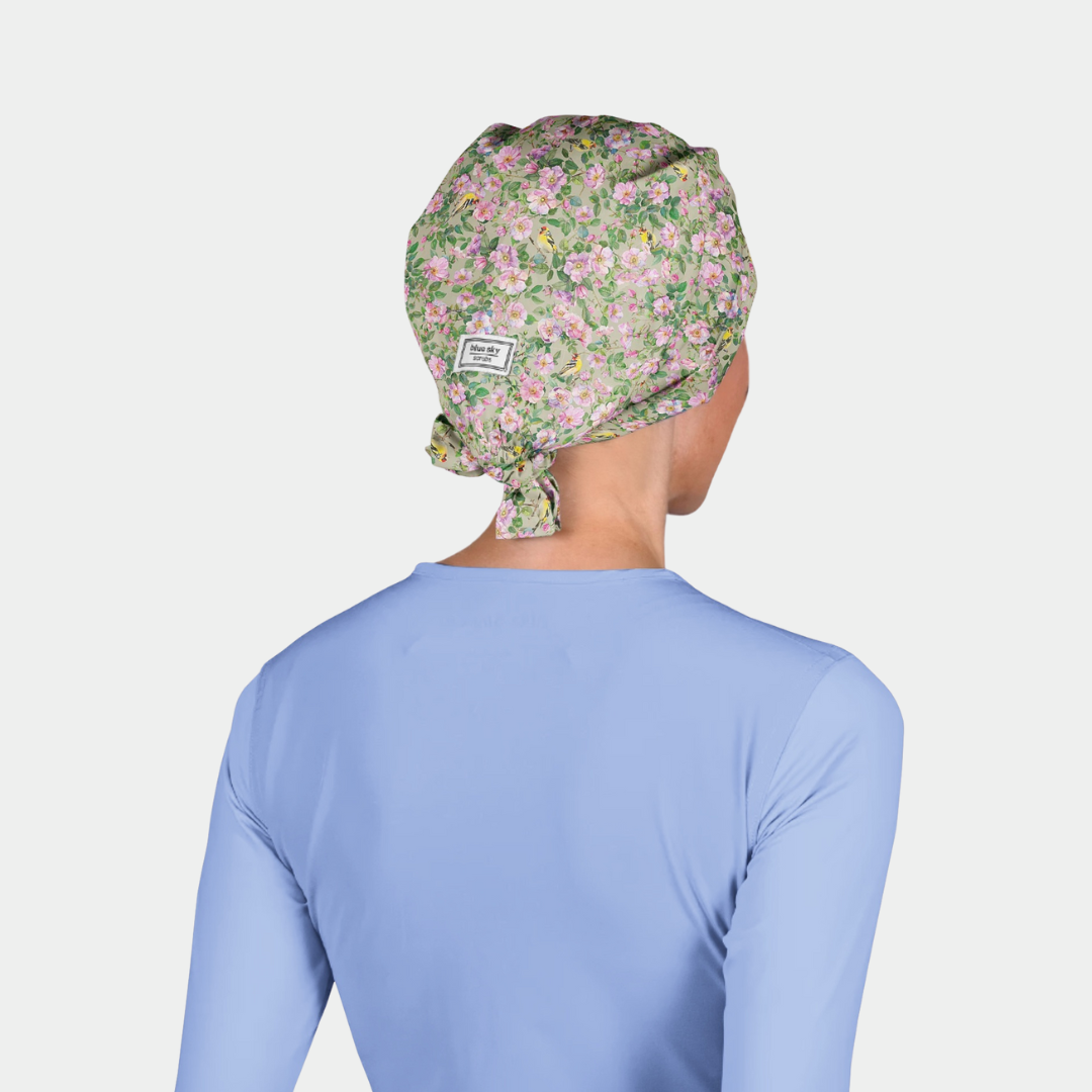 woman wearing a pastel scrub cap with flowers and leaves and a light blue scrub top on a white background
