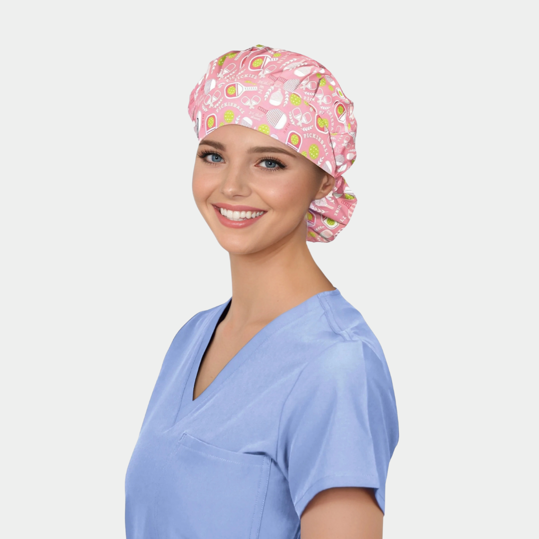 Woman wearing a pink pickleball patterned bouffant scrub cap and blue scrubs on a light gray background