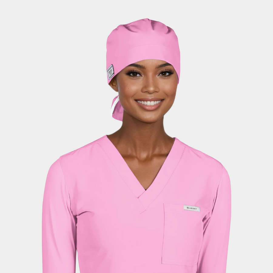 Person wearing a pink scrub top and matching scrub cap on a light gray background