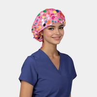 Person wearing a pink polka dot bouffant scrub cap and blue scrub top on a light gray background