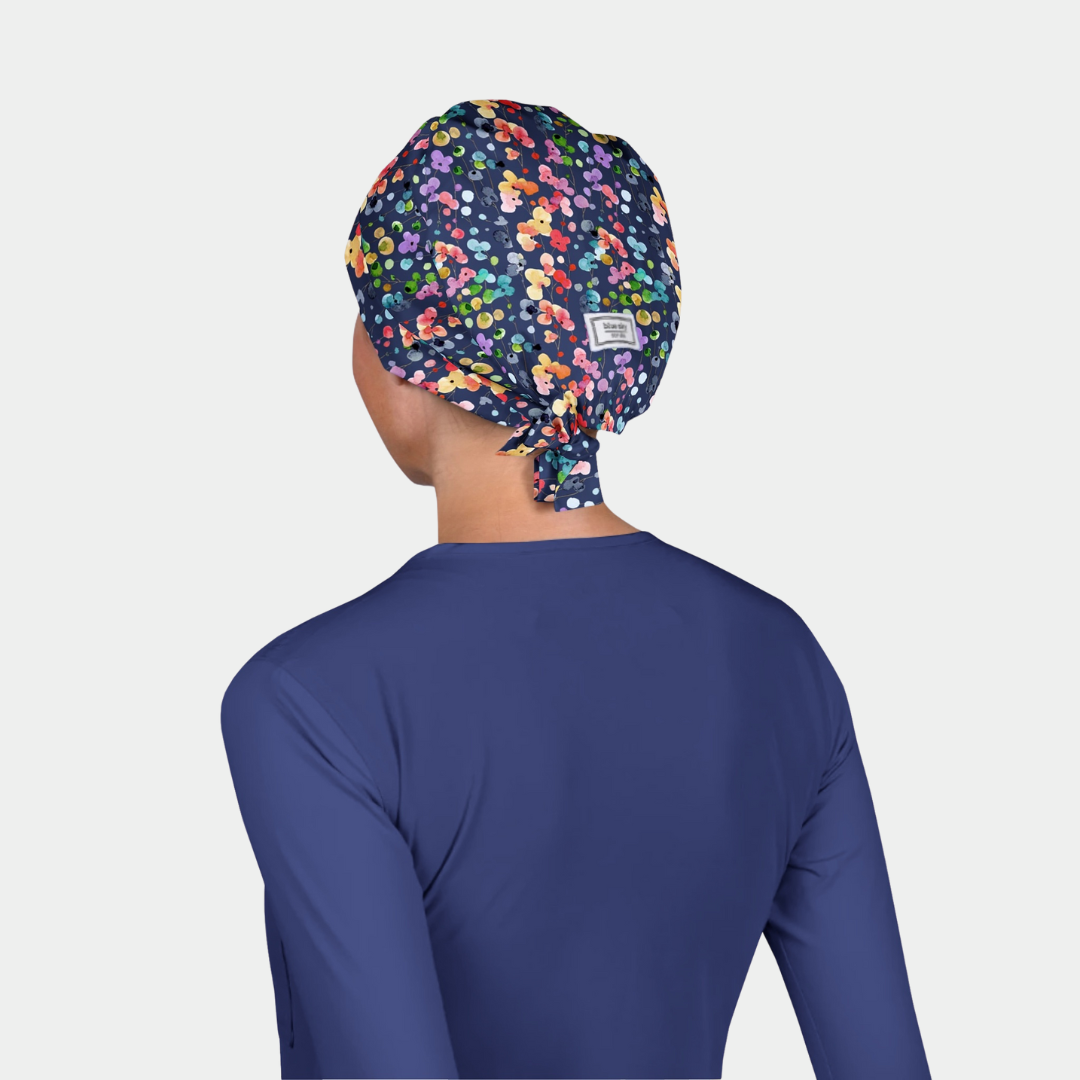 Person wearing a blue scrub top and colorful patterned scrub cap on a light gray background