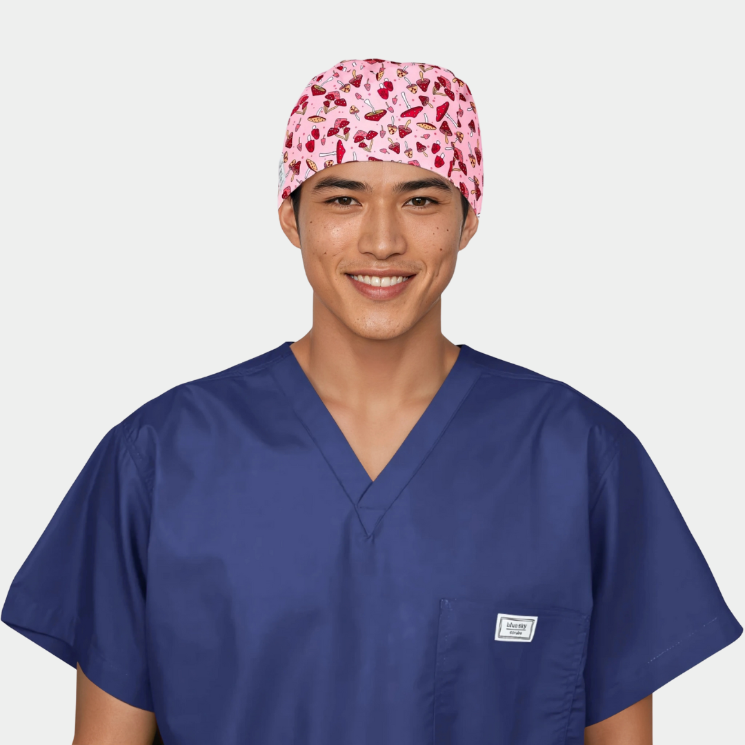 Person wearing a blue scrub top and pink mens scrub cap with red and white mushrooms on it on a white background