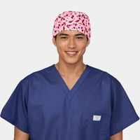 Person wearing a blue scrub top and pink mens scrub cap with red and white mushrooms on it on a white background