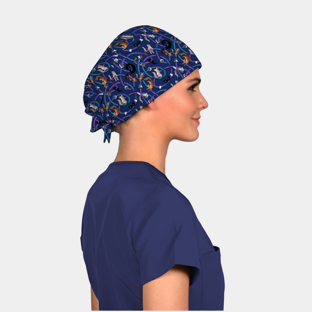 Person wearing a navy blue scrub cap with cats on it a pattern on a plain background