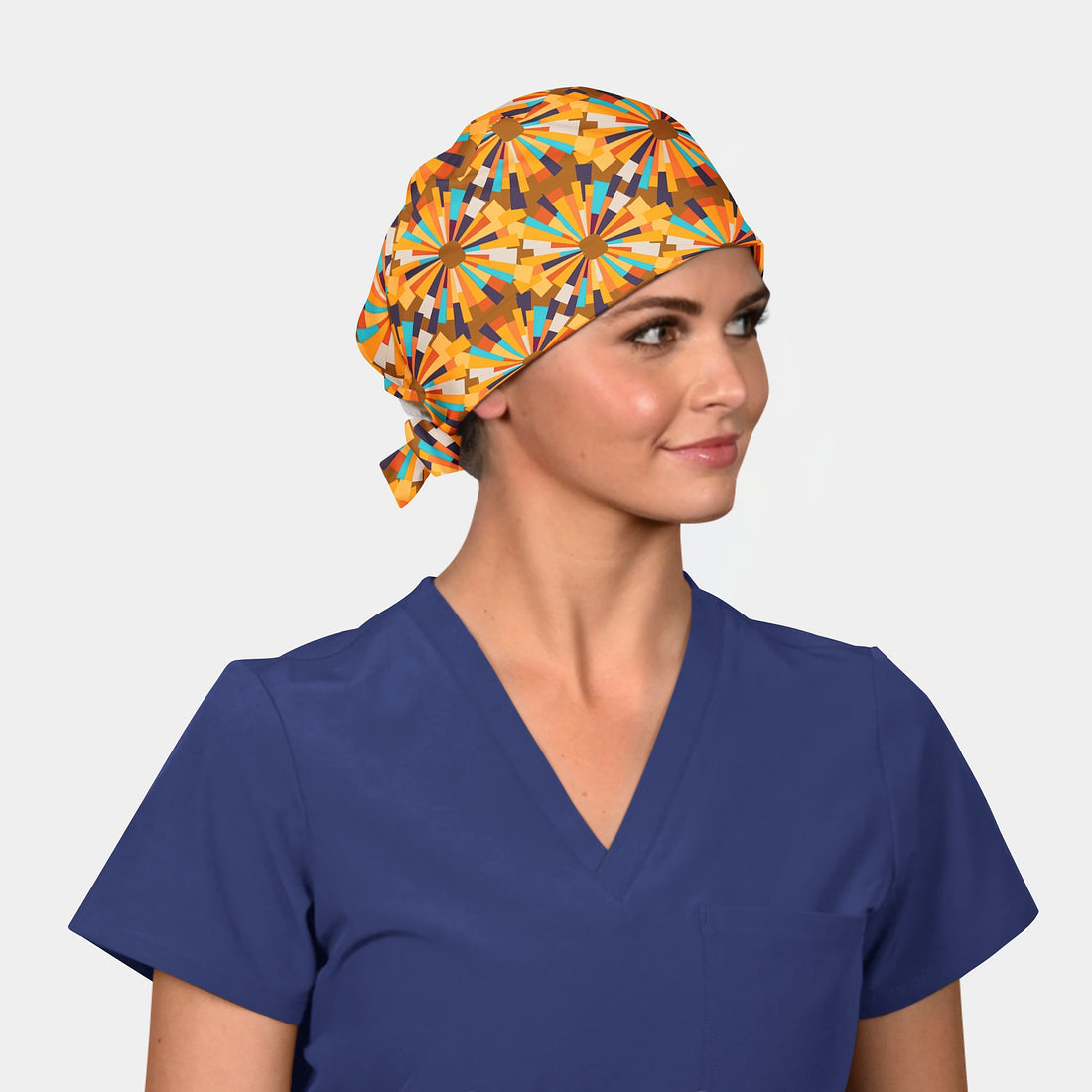 a woman with a scrub hat on that has an abstract pattern with a yellow and orange starburst pattern and a navy blue scrub top on.