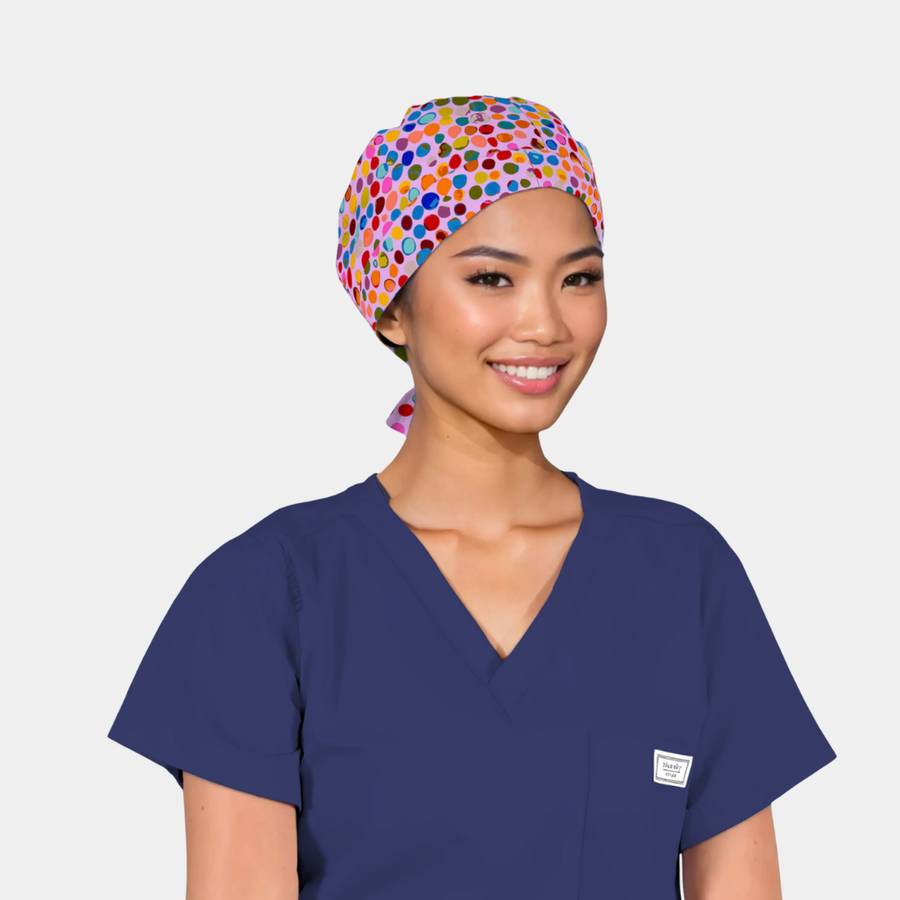 Person wearing a blue scrub top and colorful polka dot scrub cap on a plain background