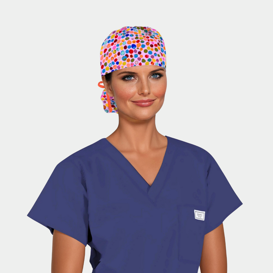 woman wearing a navy blue scrub top and a pink ponytail scrub cap with colorful dots on it