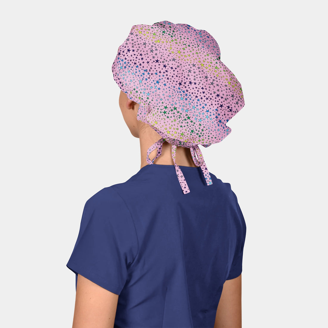 woman wearing a navy blue scrub top and a pink bouffant scrub cap with stars all over it on a white background