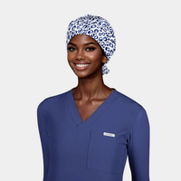 Woman wearing a blue scrub top and leopard patterned surgcial cap on a white background