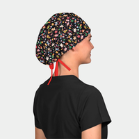 woman wearing a black scrub top and a christmas scrub cap that is black with toys on it and a red ribbon on a white background