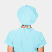 Person wearing a light blue scrub set with a matching light blue bouffant scrub cap on a white background