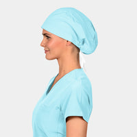 Woman wearing a light blue scrub top and matching scrub hat on a plain background