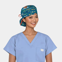 Person wearing a blue scrub top and patterned scrub cap with a noah's ark theme on a plain background