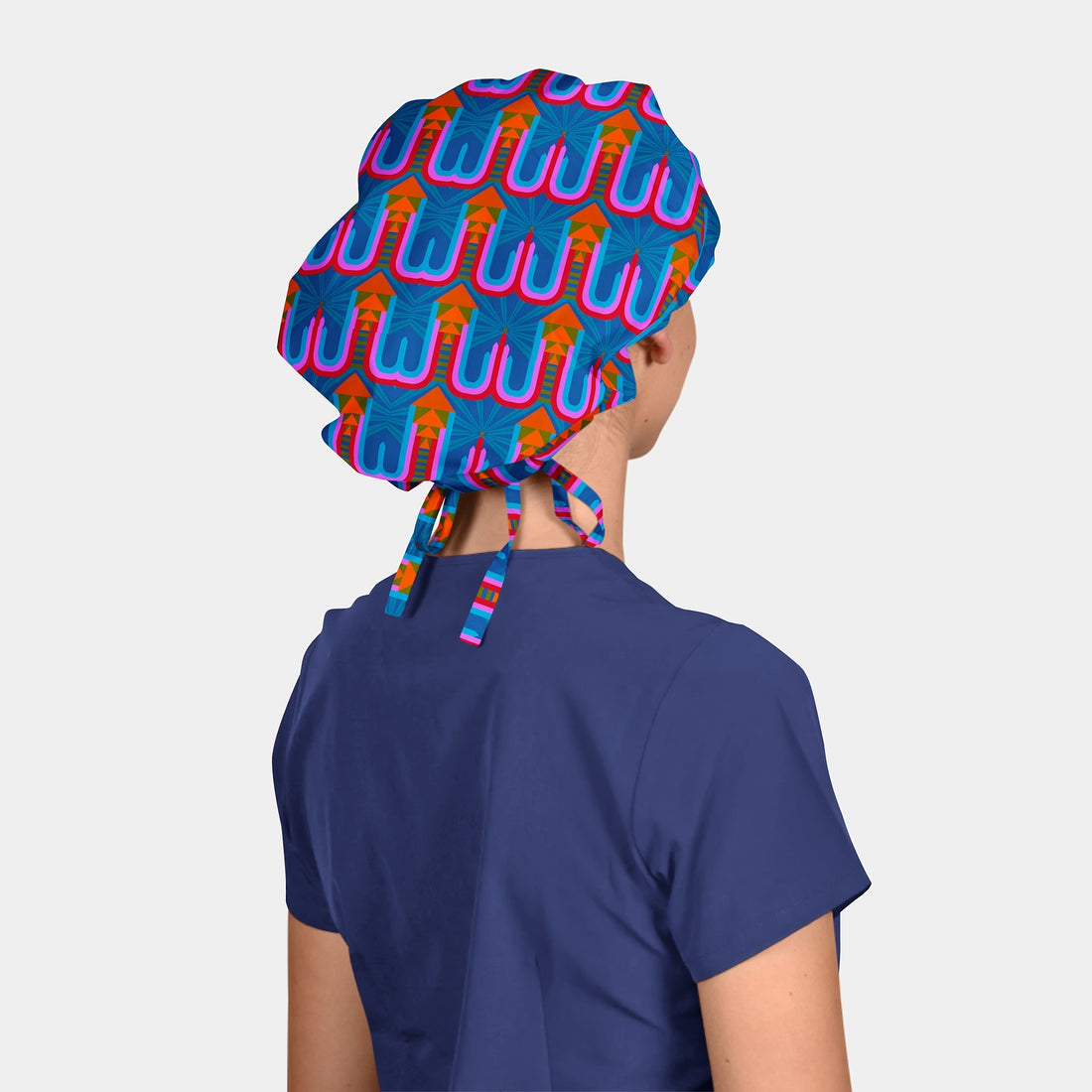 woman wearing a bouffant scrub hat that has an abstract pattern in blue, orange and pink with a navy blue scrub top on a light grey background
