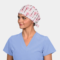 woman wearing a light blue scrub top and a scrub hat that has pink guitars on it on a white background.