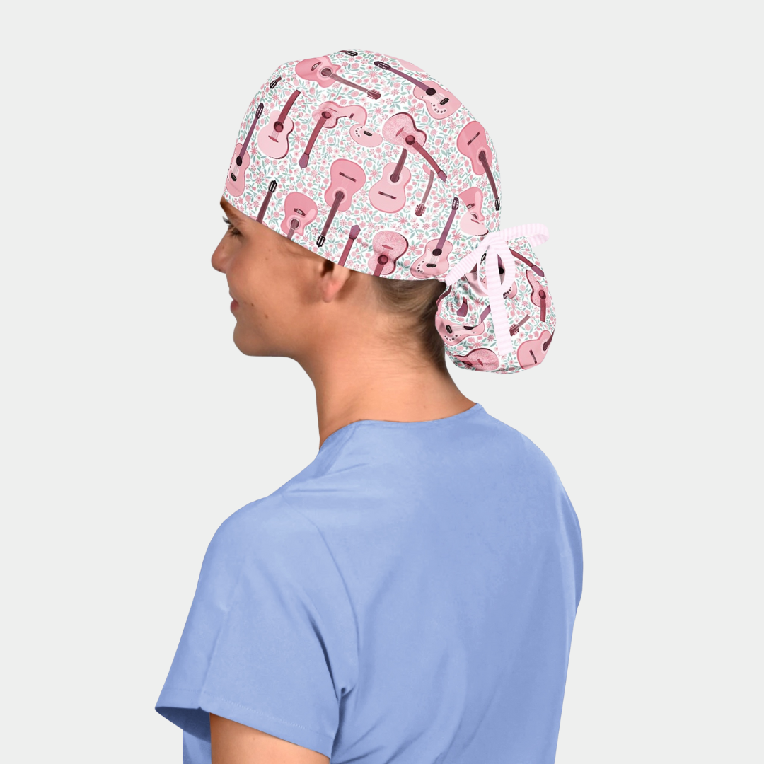 woman wearing a light blue scrub top and a ponytail scrub cap with pink guitars on a white background
