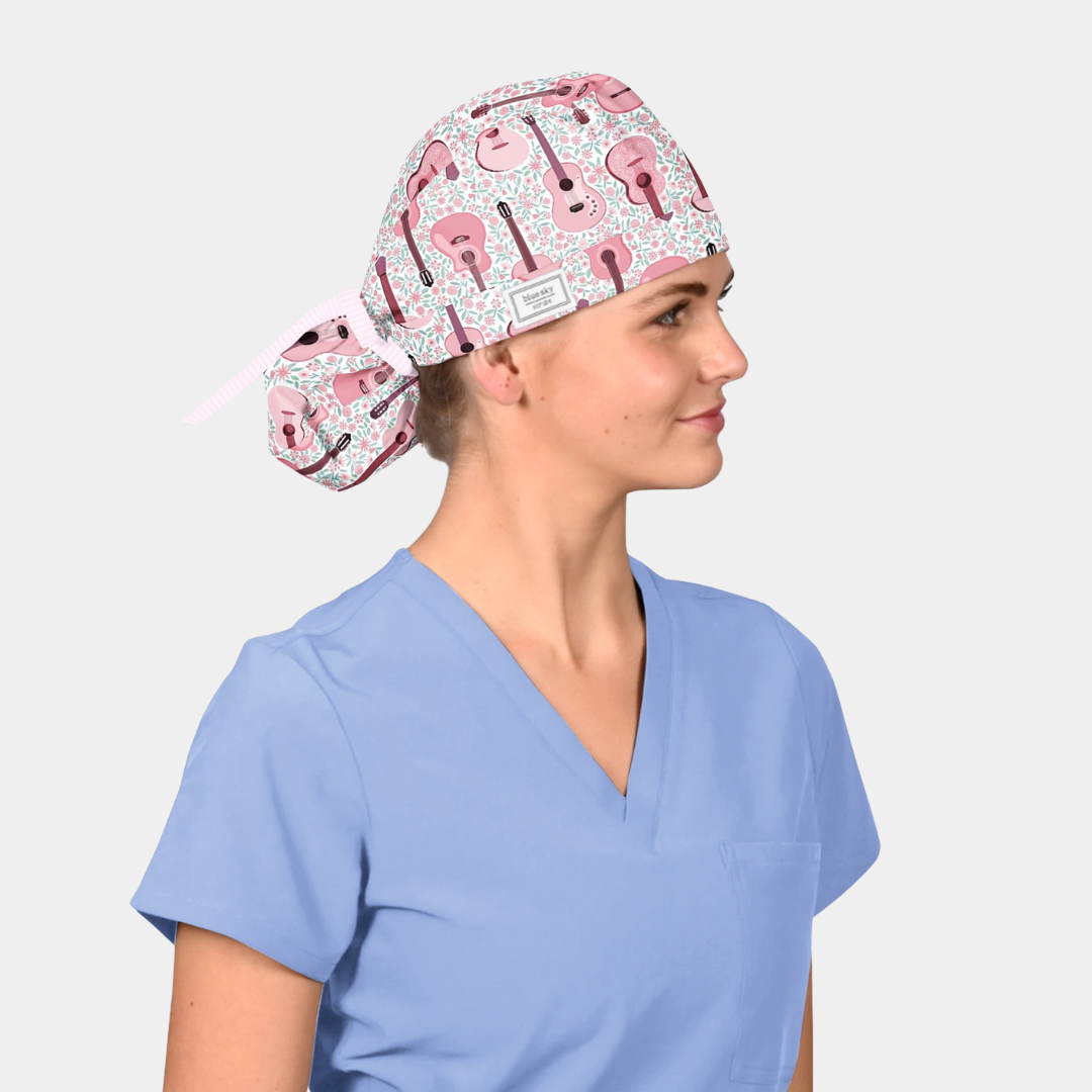 woman wearing a light blue scrub top and a ponytail scrub hat that has pink guitars on a white background.