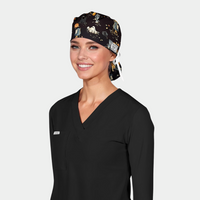woman wearing a black scrub top with a halloween themed surgical hat that is black with cats, ghosts and scarecrows