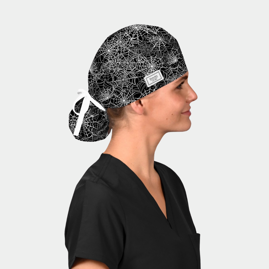 girl in a black scrub top with a halloween ponytail scrub hats on that is black with white spiderwebs and has a white ribbon