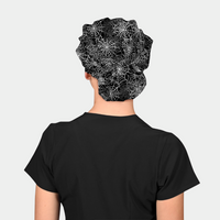 woman wearing a halloween scrub hat with white spiderwebs on a black background and a black scrub top