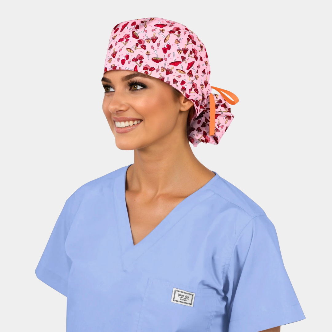 woman wearing a light blue scrub top and a pink ponytail scrub cap with red mushrooms on a white background