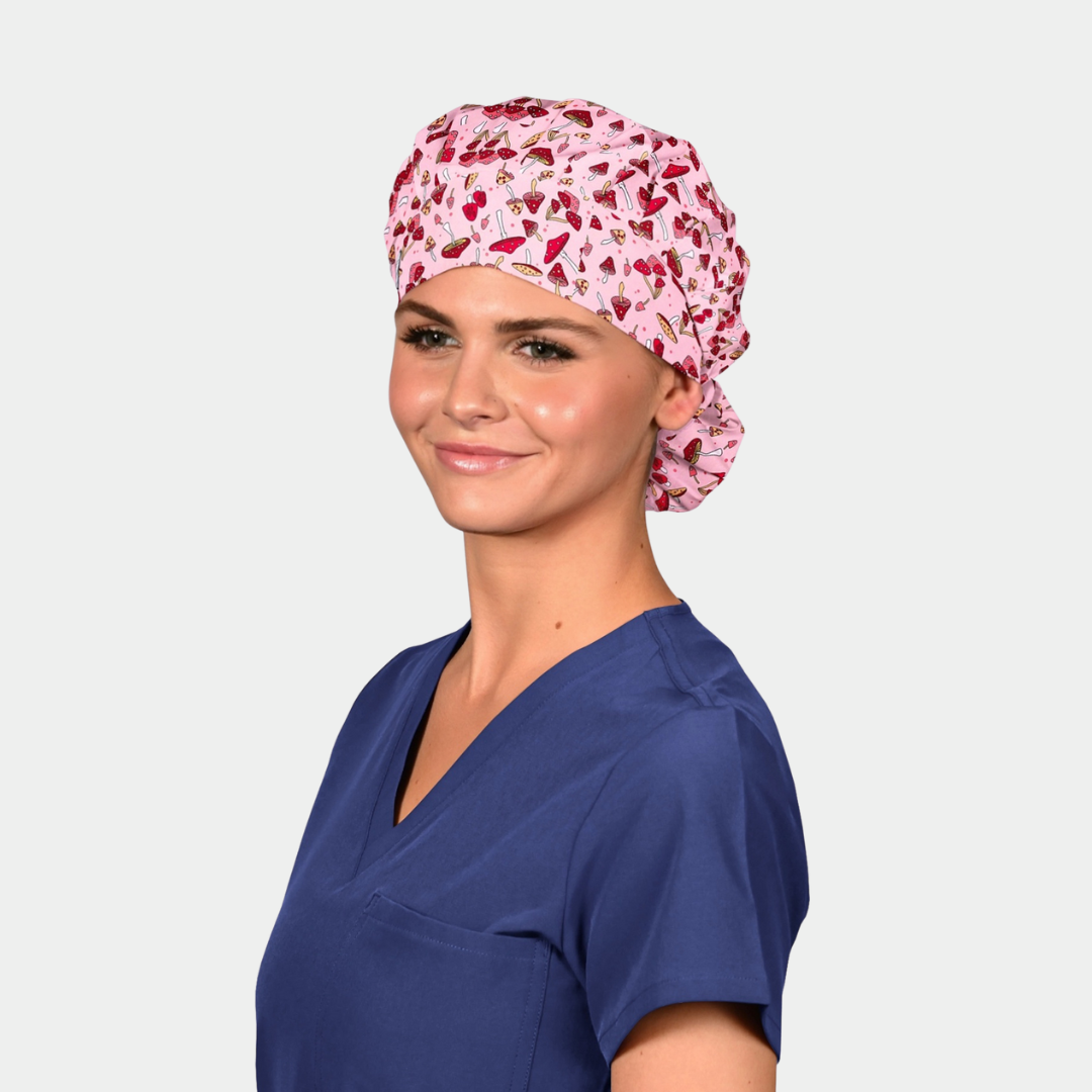 woman wearing a navy blue scrub top and a pink bouffant hat with red mushrooms on it on a white backgroun