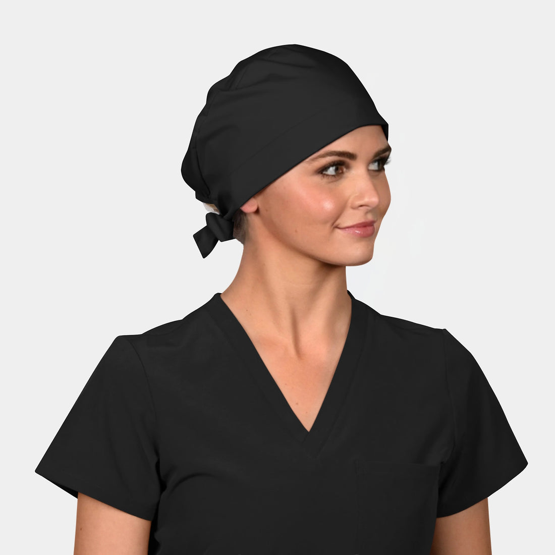 woman wearing a solid black scrub hat with a black scrub top on a light grey background